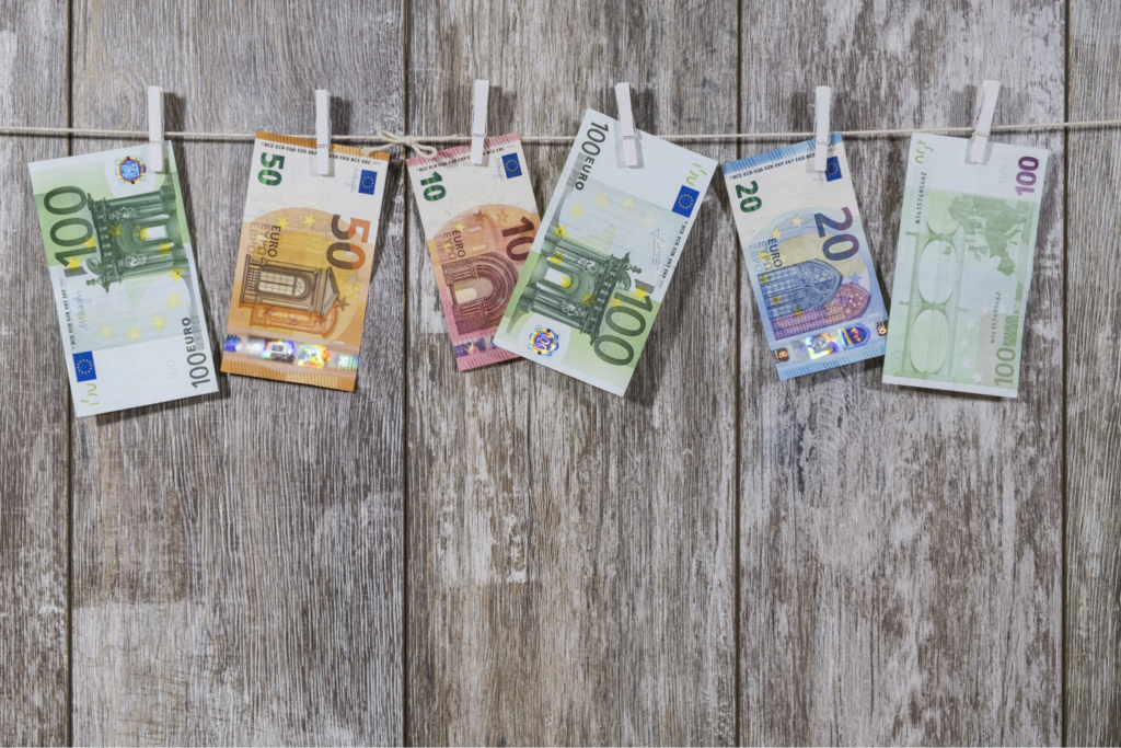 Mehrere Euro-Geldscheine hängen an einer Wäscheleine mit Wäscheklammern vor einem rustikalen Holzhintergrund.